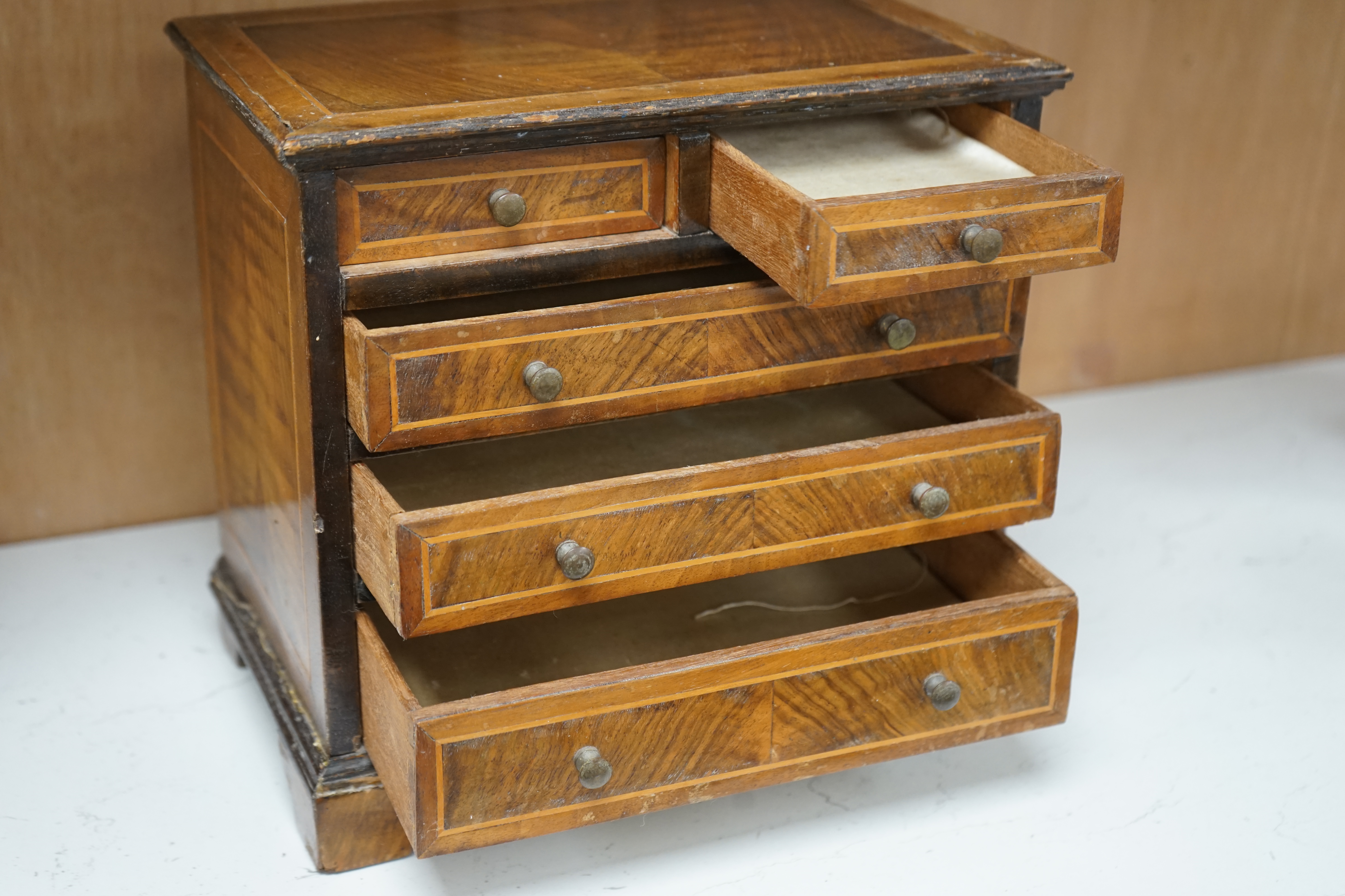 A miniature three long and two short inlaid chest of drawers, 21.5cm high x 23.5cm wide. Condition - poor to fair